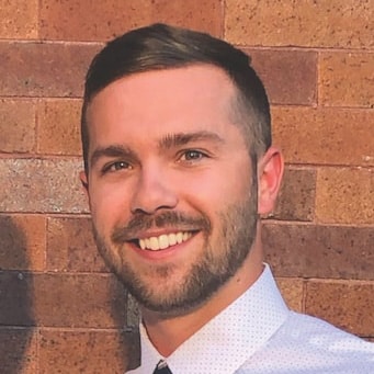 A man smiling in front of a brick wall.