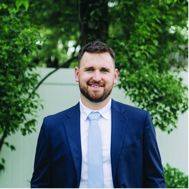 A man in a suit and tie standing in front of a tree.