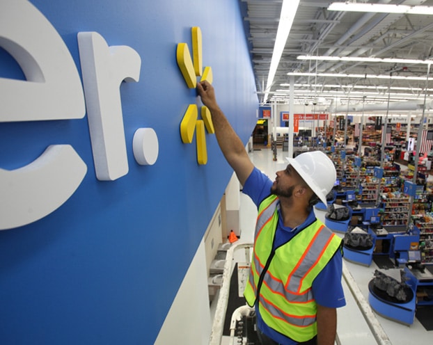 A worker is painting a sign at a walmart store.