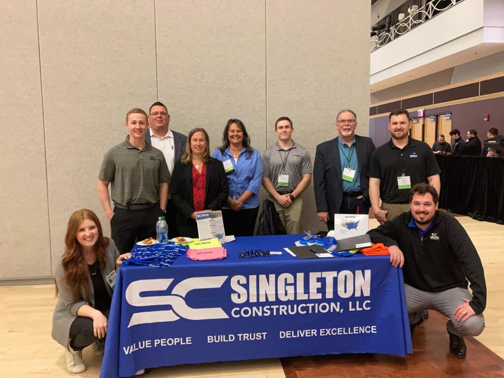 A group of people standing in front of a table with a sign for singleton construction llc.